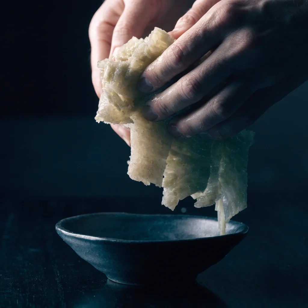 Tangan menyobek sauerkraut di atas mangkuk keramik gelap di meja kayu hitam